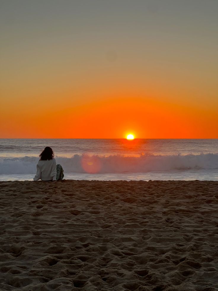 a person sitting alone on the beach during sunset