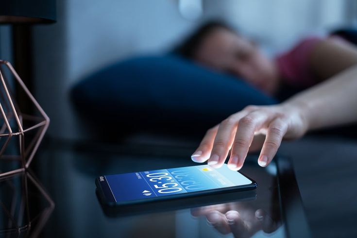 A woman reaching out for phone to snooze the alarm