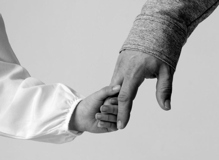 A child's hand reaches for a father's finger.
