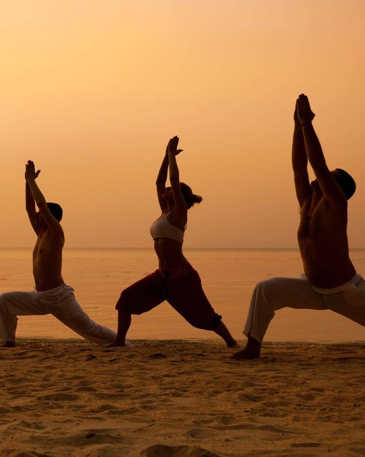 three people performing yoga during sunset on a beach